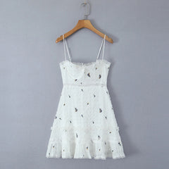 White lace dress with floral embroidery on a wooden hanger against a gray background