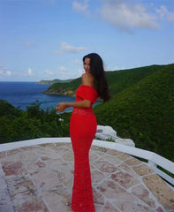 Woman in a red dress standing on a stone platform with ocean and green hills in the background