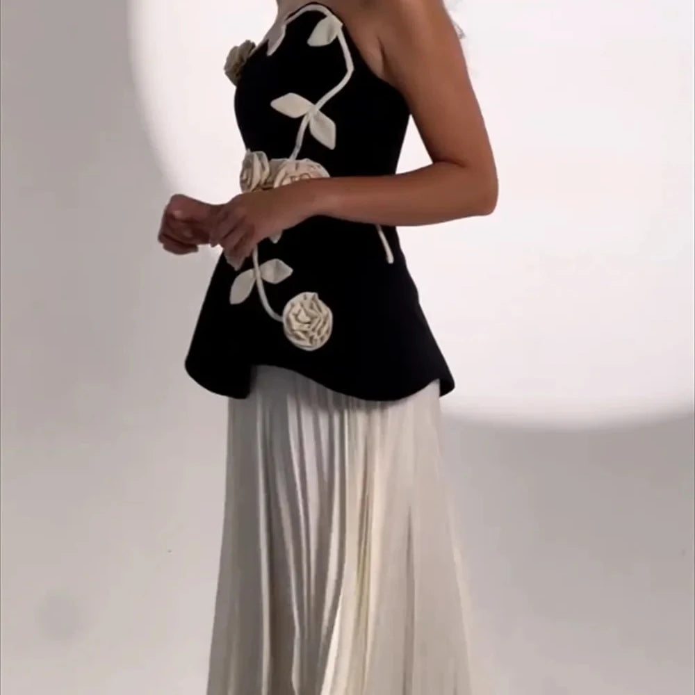 Black top with floral designs and white pants on a plain background