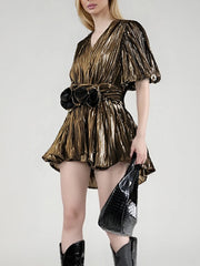 Woman wearing a gold metallic dress with a black belt and holding a matching handbag on a white background