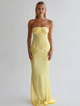 Woman wearing a strapless yellow evening gown against a plain background