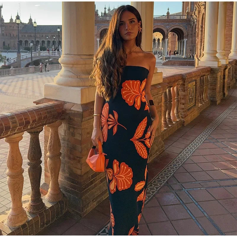 Woman in a strapless dress with orange floral patterns standing in an outdoor setting with columns and architecture.