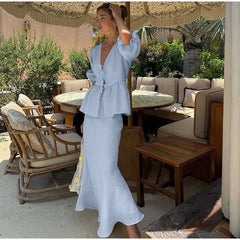 Woman in a light blue dress standing in an outdoor setting with tables and chairs.