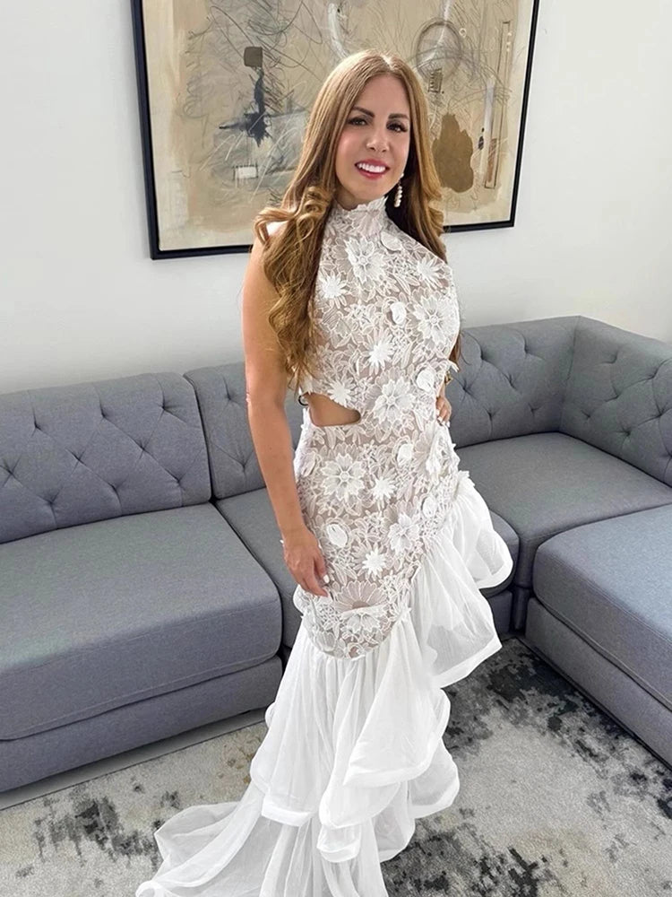 Woman in a white lace dress standing in a living room with a gray sofa and abstract art on the wall.