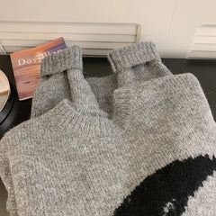 Gray knit sweater with a black design on a surface next to a book.