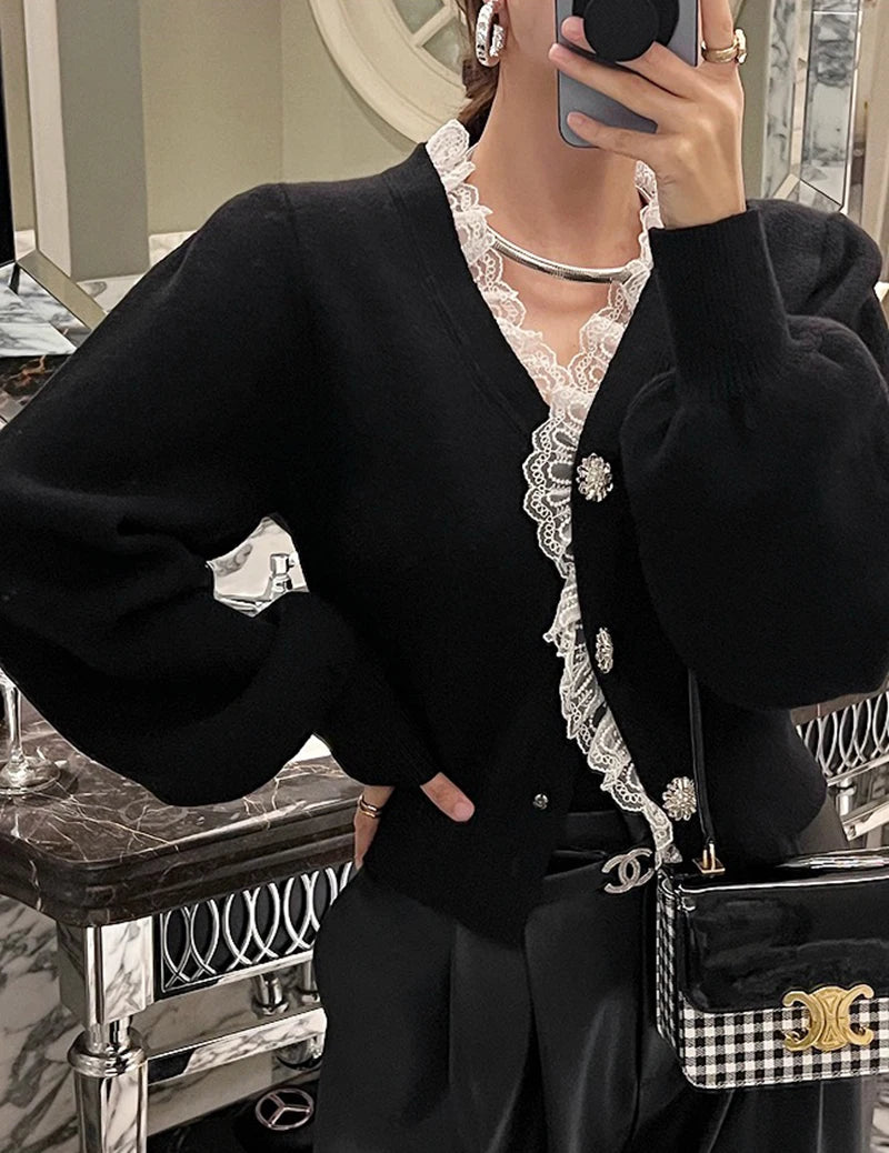 Person wearing a black cardigan with lace details, holding a checkered handbag.