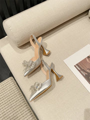 Silver high-heeled shoes with embellishments on a beige surface.