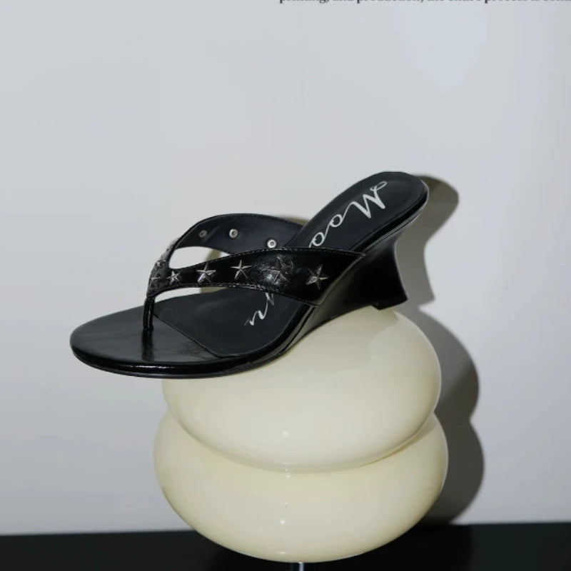 Black wedge sandal with star embellishments on a display stand