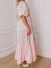 Woman wearing a pink floral dress standing against a white paneled wall.