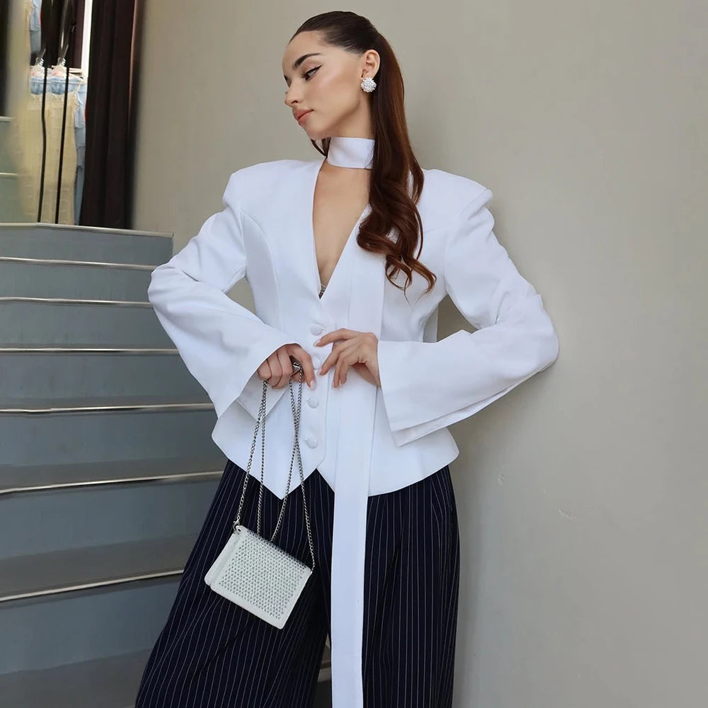 Woman in a white blazer and black pants holding a white handbag on a staircase.