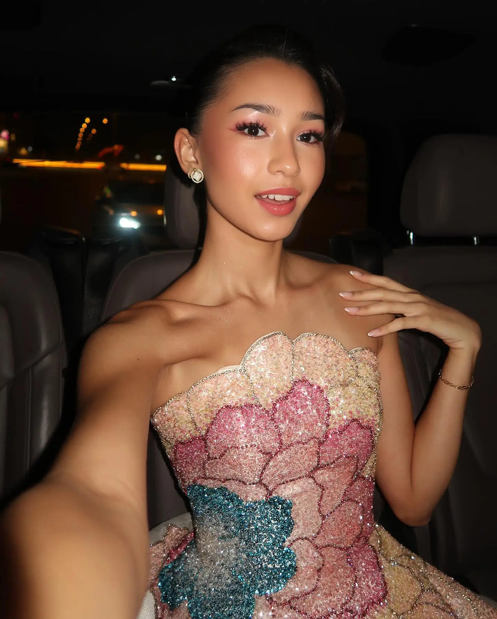Woman in a sparkling dress inside a vehicle at night.