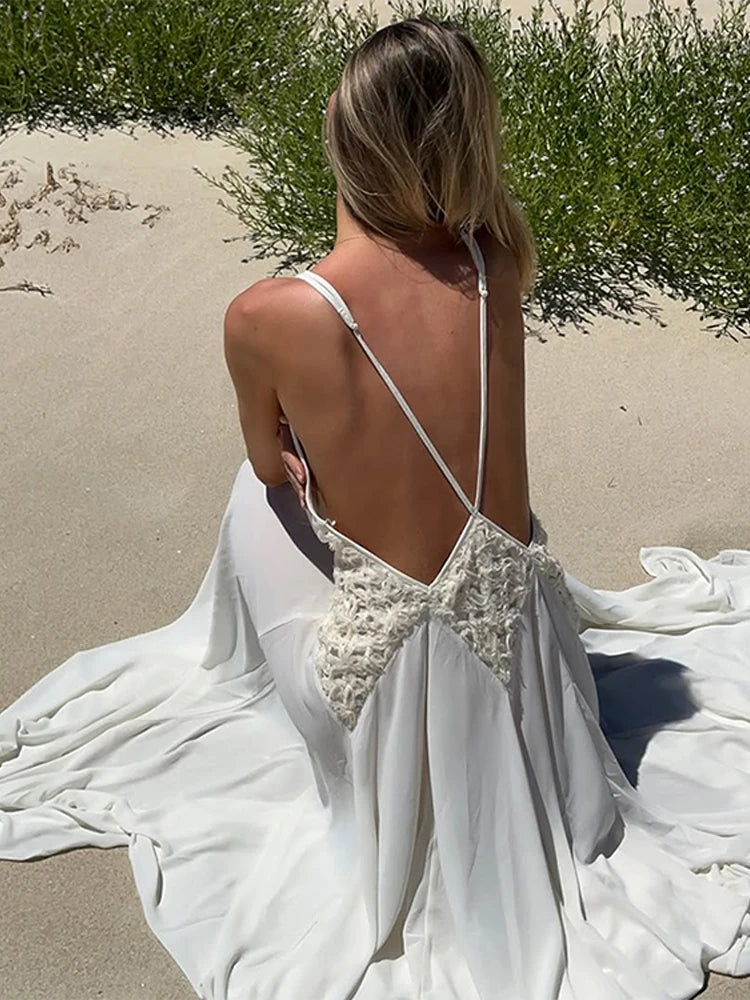 Woman in a white wedding dress with floral back design on a sandy beach.