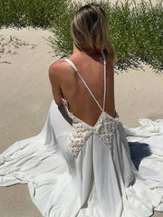 Woman in a white wedding dress with floral back design on a sandy beach.