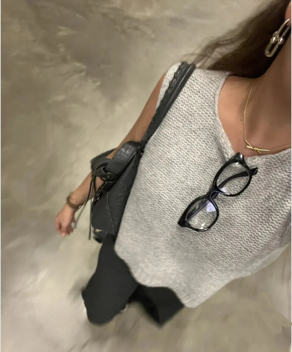 Person wearing a textured sleeveless top with a black handbag and glasses on a neutral background