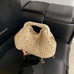 Beige woven handbag held by a person in front of a black leather couch.