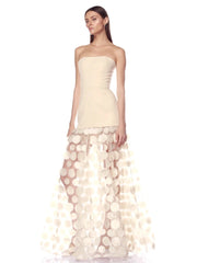 Woman wearing a strapless dress with a sheer, circular patterned overlay on a white background