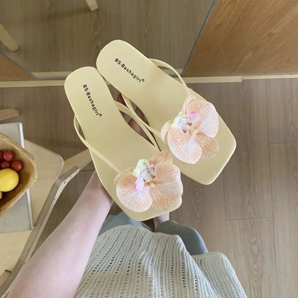 Beige sandals with floral decorations held by a person indoors.