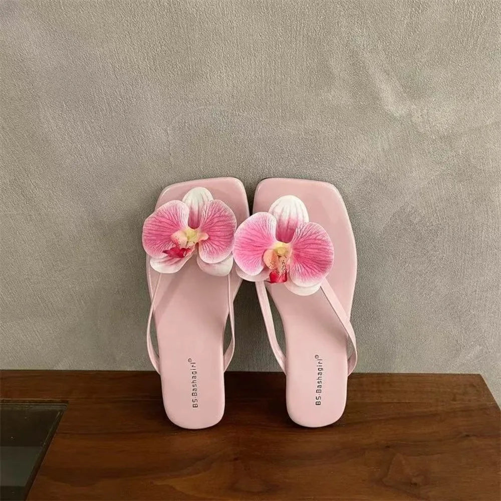 Pink sandals with floral decorations on a wooden surface and gray background