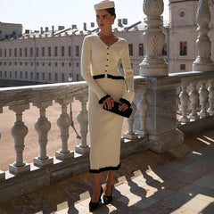 Woman in a white dress with black trim standing on a balcony with classical architecture.