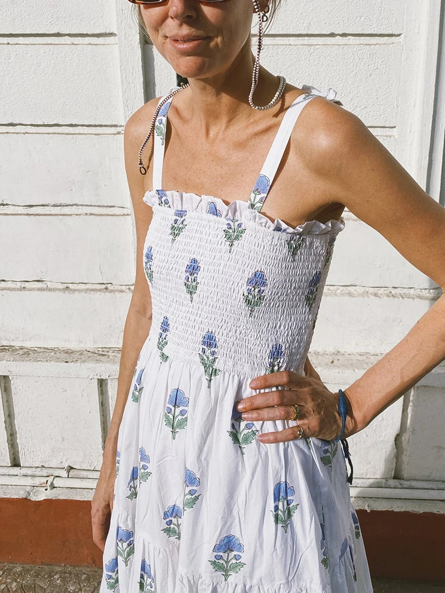 Woman wearing a white floral dress against a white wall.