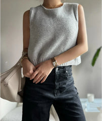 Person wearing a gray sleeveless top and black jeans, holding a beige handbag.