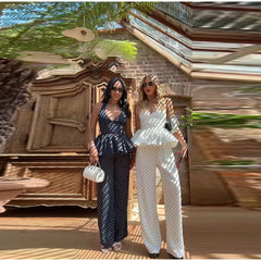 Two women posing outdoors with a decorative wall and plants in the background