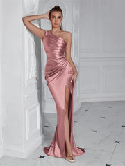 Woman wearing a pink satin one-shoulder dress with a slit in a white room.