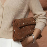 Brown studded clutch held by a person wearing a beige sweater.