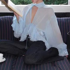 Sheer ruffled halter blouse on a woman sitting on a couch, holding a book.