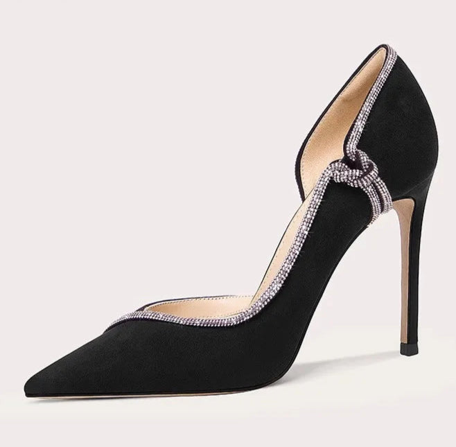 Black high-heeled shoe with decorative strap on a light gray background
