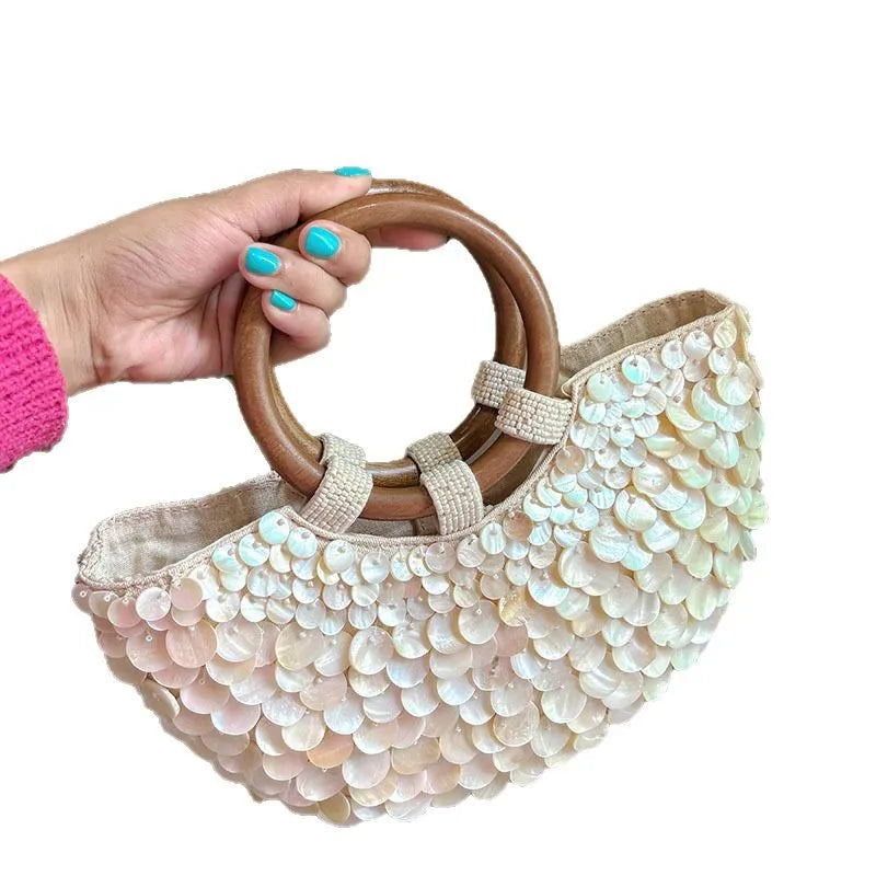 Hand holding a beaded handbag with wooden handles on a white background