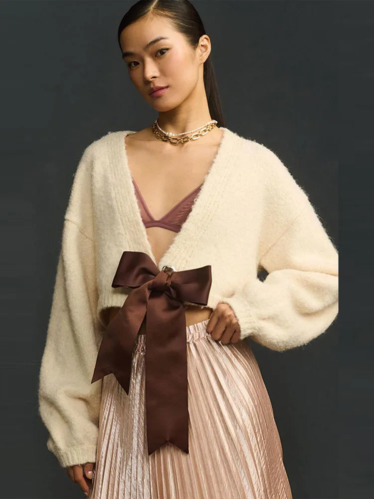 Woman wearing a cream cardigan with a large brown bow and a dark background