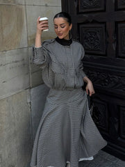Woman in a checkered dress holding a coffee cup against a stone wall.