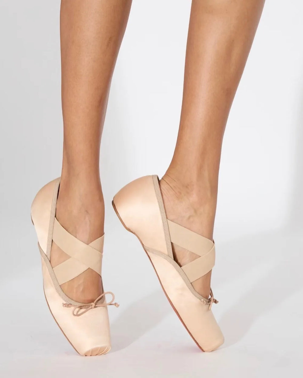 Beige ballet shoes worn by a person on a light gray background