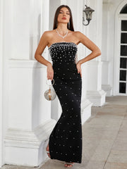 Woman in a black strapless dress with white embellishments standing in front of a white building.