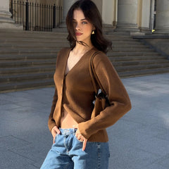 Woman in a brown cardigan and blue jeans standing outdoors with steps and columns in the background