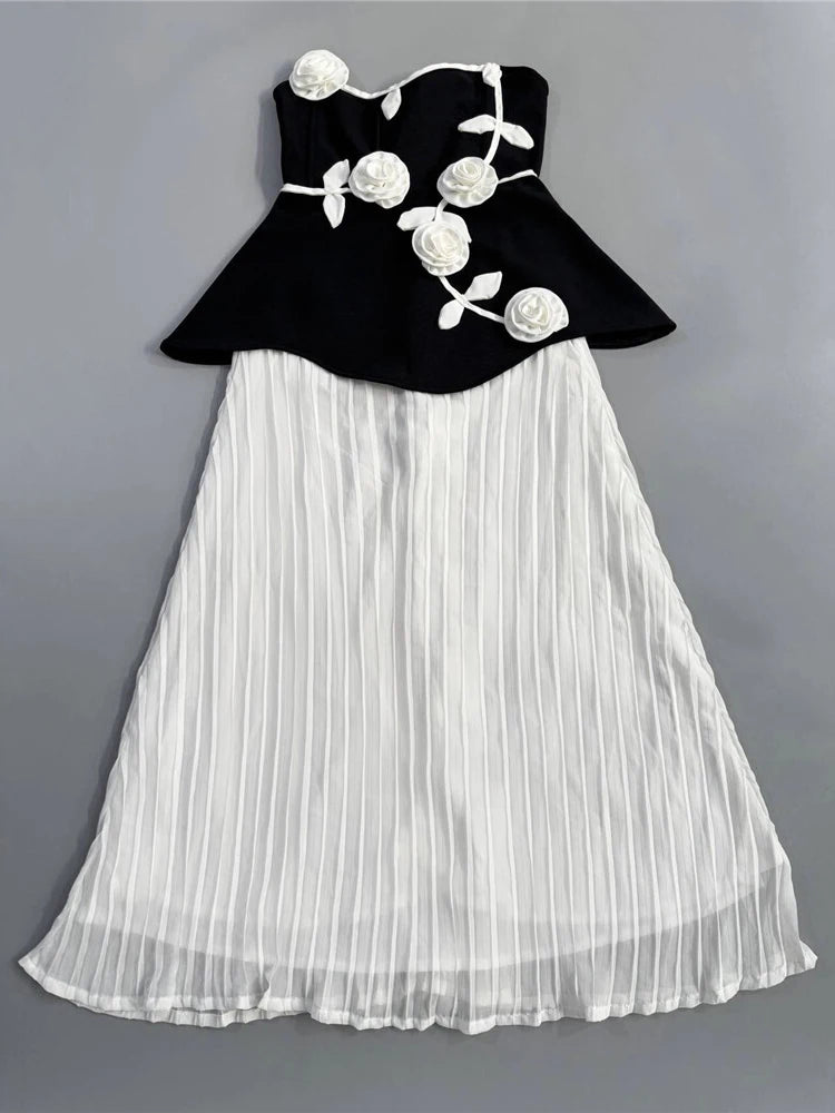 Black top with floral designs and white pleated skirt on a gray background