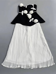 Black top with floral designs and white pleated skirt on a gray background