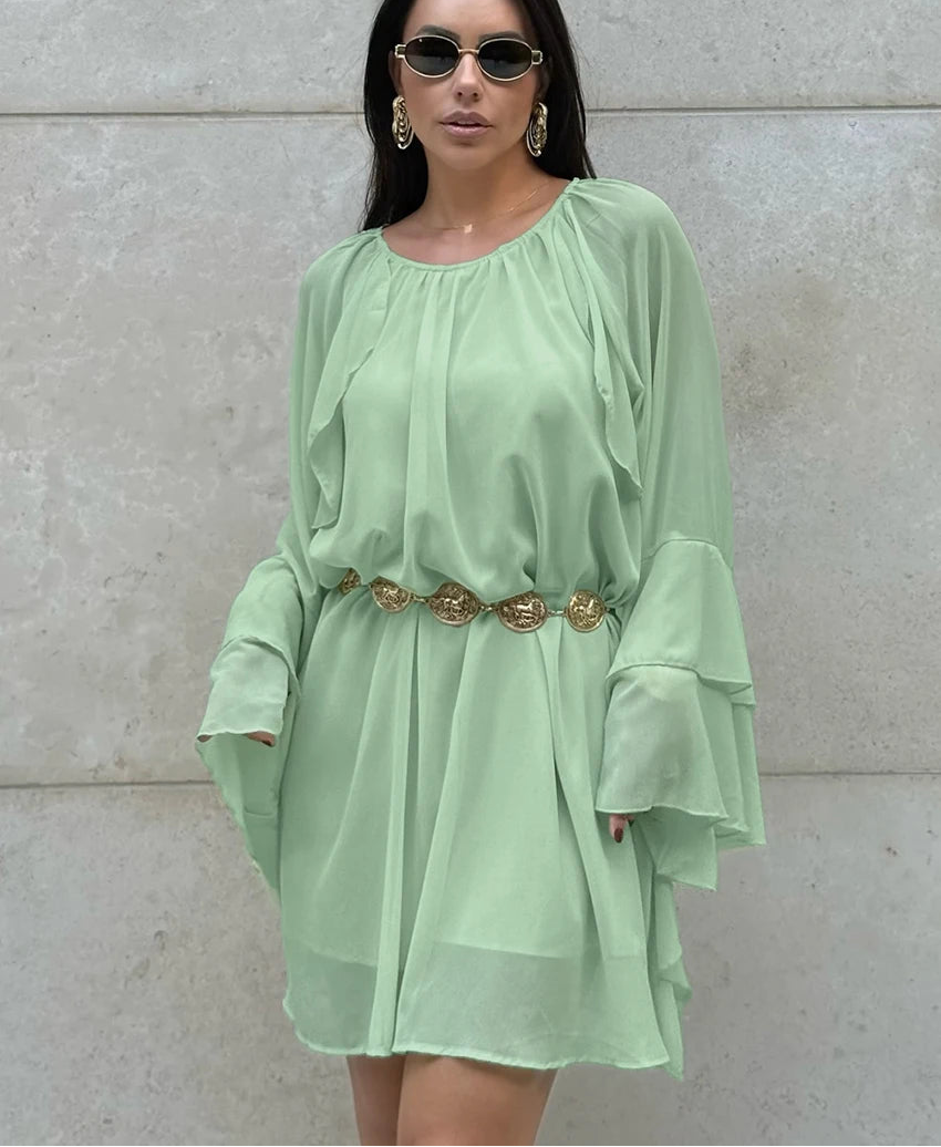 Woman wearing a light green dress with a belt against a gray wall