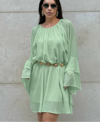 Woman wearing a light green dress with a belt against a gray wall