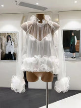 Mannequin wearing a white sheer blouse with ruffled details in an indoor setting.
