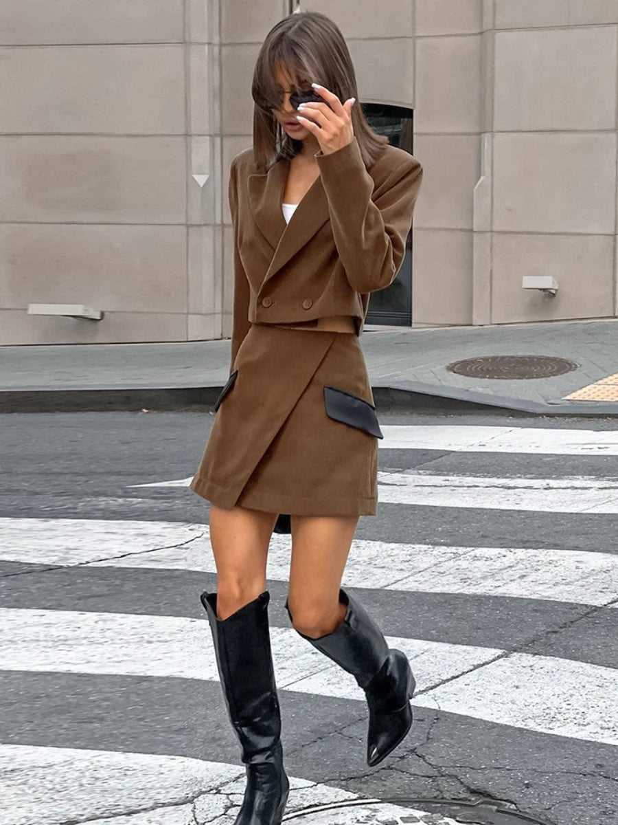 Woman taking a mirror selfie wearing a brown outfit with black knee-high boots on a city street.