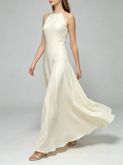 Model wearing a flowing halter neck a-line maxi dress with a pleated skirt.