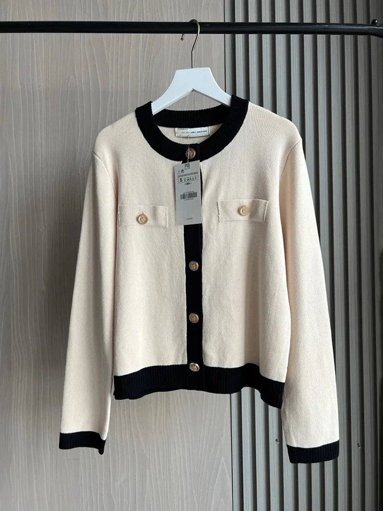 White cardigan with black accents on a hanger against a striped background