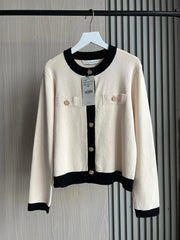 White cardigan with black accents on a hanger against a striped background
