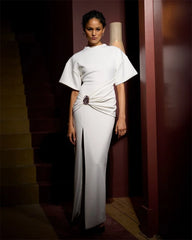 Woman wearing a white dress with a draped front in a dimly lit room.