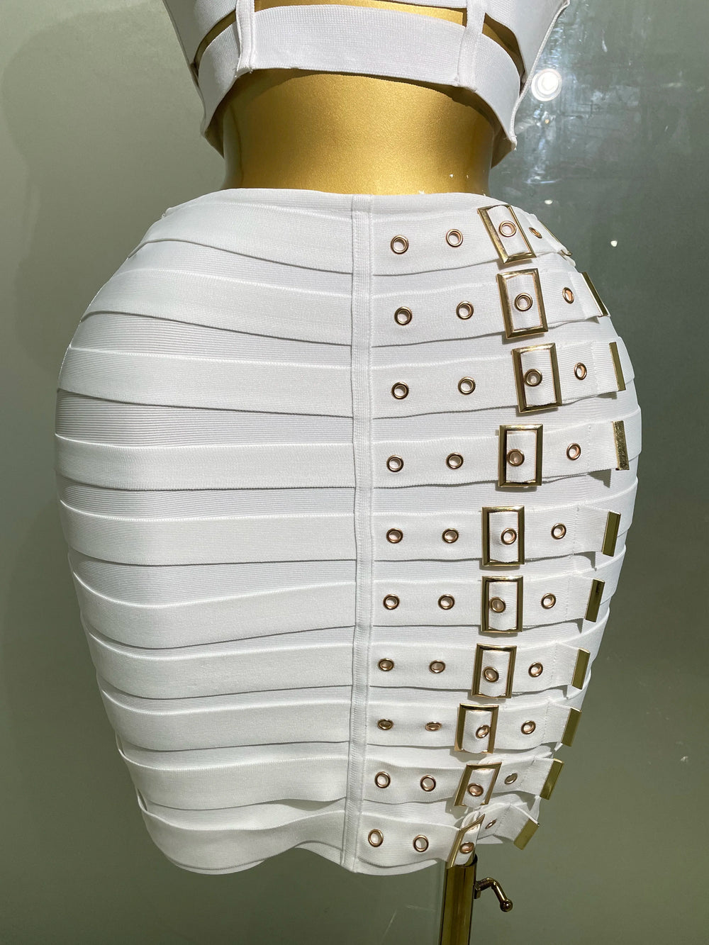 White skirt with gold buckles on a mannequin against a neutral background