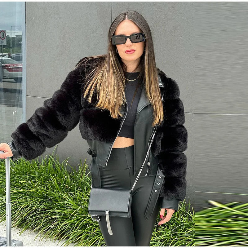 Woman in a black fur jacket and sunglasses standing outdoors with grass and a building in the background.