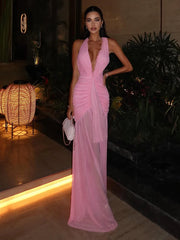 Woman in a pink dress standing outdoors with plants and lights in the background