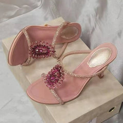 Pink thin heel sandals with crystal accents on a box.